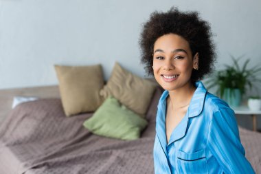 Yatak odasındaki kameraya gülümseyen pijamalı Afro-Amerikalı kadın. 