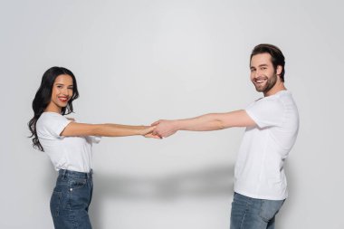 Beyaz tişörtlü neşeli bir çift gri tişörtü tutarken kameraya bakıyor.