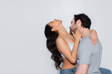 Genç adam, gri gözleri kapalı seksi esmer kadına sarılıyor.