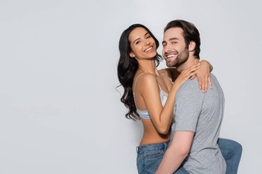 Mutlu ve seksi çift kameraya bakarken gri renkte izole edilmiş bir şekilde sarılıyorlar.