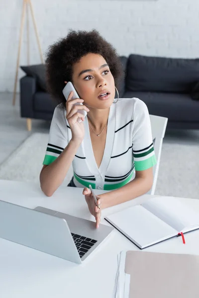 Mujer Afroamericana Hablando Teléfono Inteligente Cerca Computadora Portátil —  Fotos de Stock