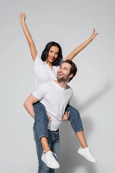 Cheerful Man Piggybacking Excited Brunette Woman White Shirt Jeans Grey — Stockfoto