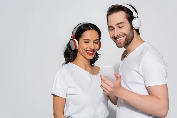 Joyful Couple White Shirts Headphones Looking Mobile Phone Grey — Stock Photo, Image