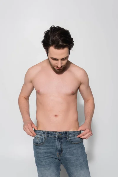 Jovem Sem Camisa Homem Tocando Jeans Enquanto Sobre Cinza — Fotografia de Stock