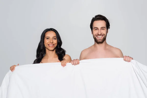 Neşeli Esmer Çift Kameraya Gülümserken Gri Üzerinde Beyaz Battaniye Tutuyorlar — Stok fotoğraf
