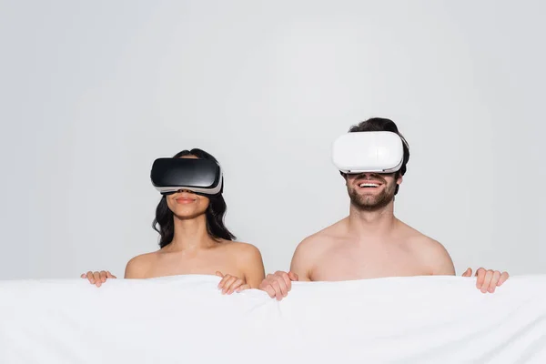 happy couple with white blanket gaming in vr headsets isolated on grey