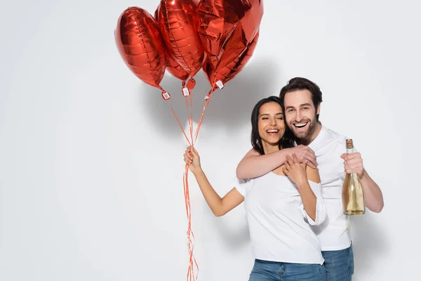 Glücklicher Mann Mit Champagnerflasche Umarmt Frau Mit Roten Herzförmigen Luftballons — Stockfoto