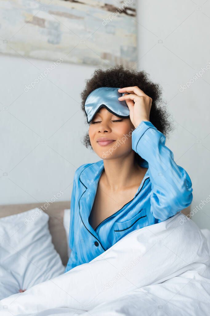 smiling african american woman in pajamas adjusting sleeping mask