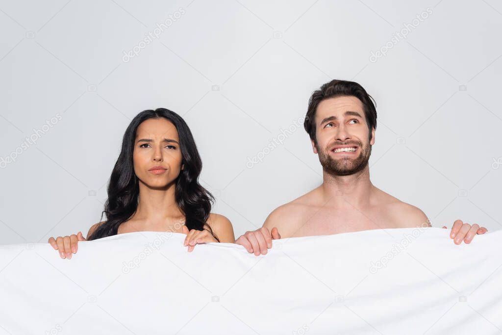 displeased woman looking at camera near confused man and white blanket isolated on grey