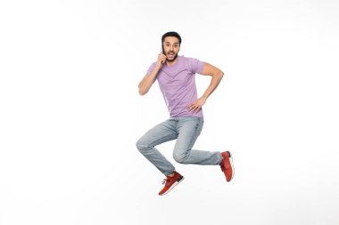 Kot pantolonlu ve mor tişörtlü bir adamın beyaz bir cep telefonuyla konuşurken havada süzülmesi. 