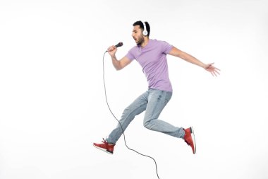 young man in wireless headphones singing in microphone and levitating on white clipart