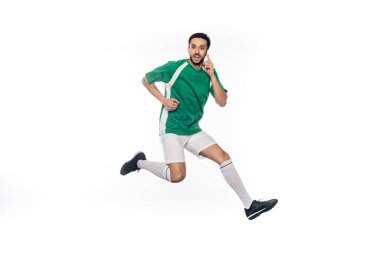 Beyazlar üzerinde izole bir şekilde akıllı telefondan konuşan üniformalı mutlu futbolcu. 