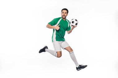 Futbol topunu tutarken ve başparmağını beyaza gösterirken üniformalı bir futbolcunun zıplaması hayret verici. 