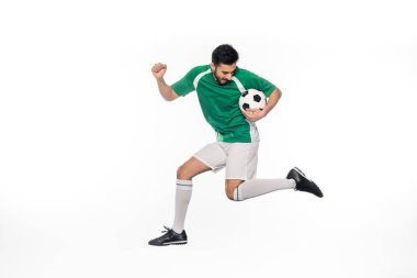 Genç futbolcu üniformalı, futbol topuyla beyaz üzerine atlıyor. 