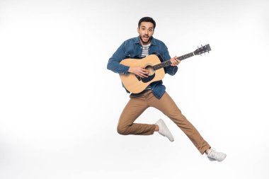 Mutlu adam akustik gitar çalarken havada süzülüyor.