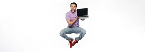 穿着牛仔裤和紫色T恤的积极向上的男人 拿着笔记本电脑挂在白色横幅上 — 图库照片