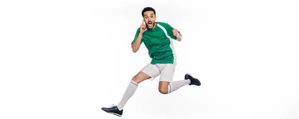 Sorprendido Jugador Fútbol Uniforme Saltando Mientras Habla Teléfono Inteligente Blanco —  Fotos de Stock
