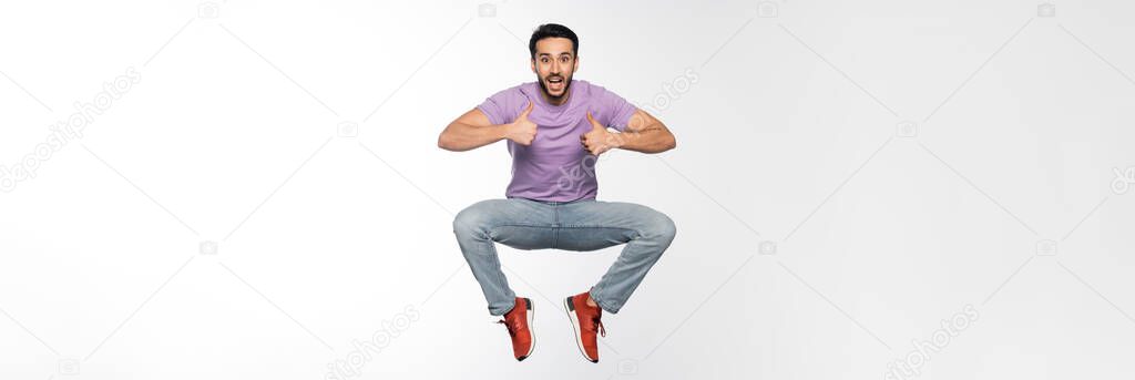 amazed man in jeans and purple t-shirt levitating while showing thumbs up on white, banner