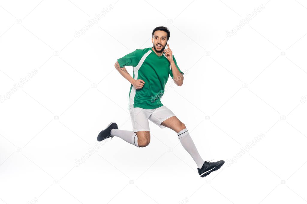 happy football player in uniform jumping while talking on smartphone isolated on white 