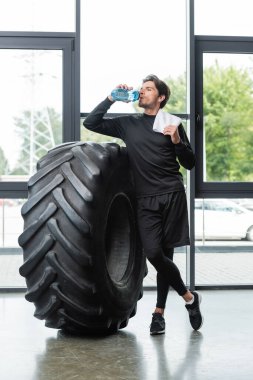 Sporcu su içiyor ve spor merkezinde lastiğin yanında havlu tutuyor. 