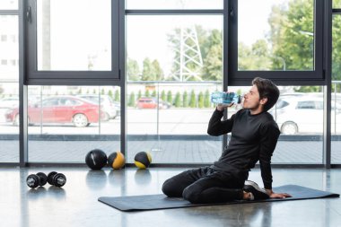Spor salonundaki dambılların yanında sporcunun spor minderinde su içişi. 