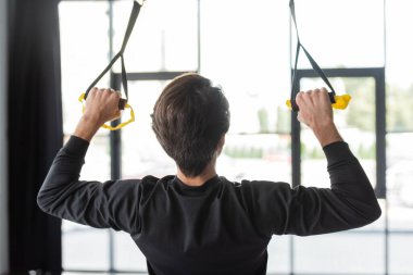 Esmer sporcunun spor salonunda antrenman yaparken süspansiyon kayışlarını çekişi.