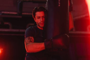 Sporcu spor salonunda kırmızı ışıkta kum torbasına sarılıyor. 