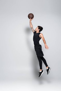 Basketbol topu gri arka planda zıplayan oyuncunun yan görünümü 