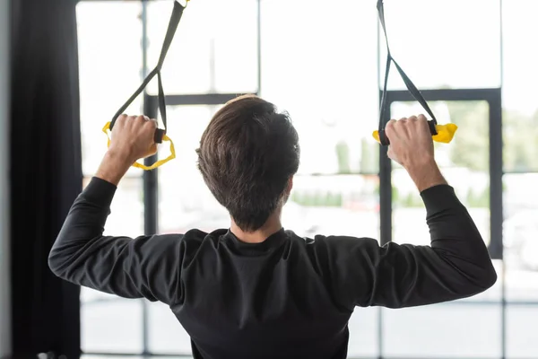 Back View Brunette Sportsman Pulling Suspension Straps While Training Gym - Stock-foto