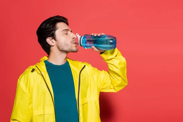 Deportista Chaqueta Deportiva Amarilla Bebiendo Agua Sobre Fondo Rojo — Foto de Stock