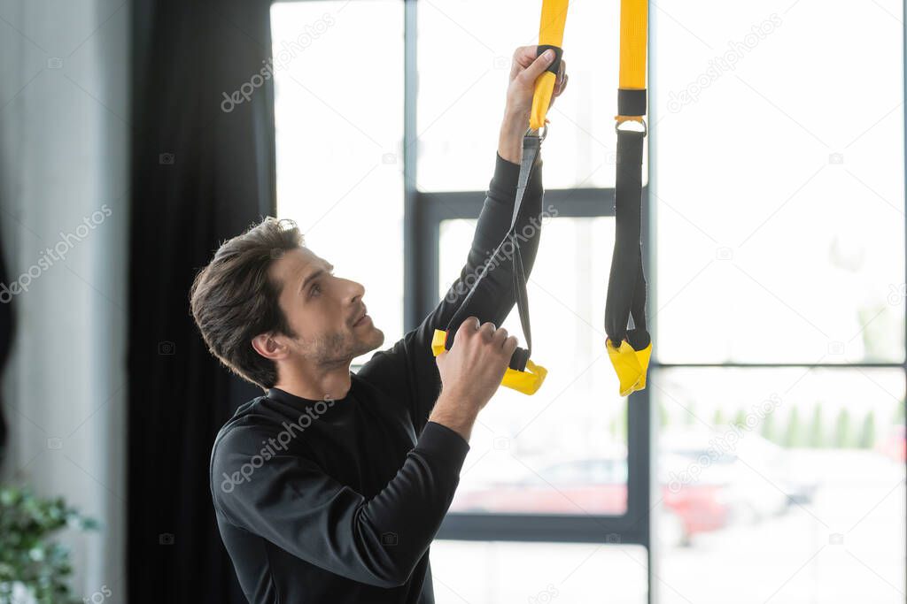 Brunette sportsman adjusting suspension straps in gym 