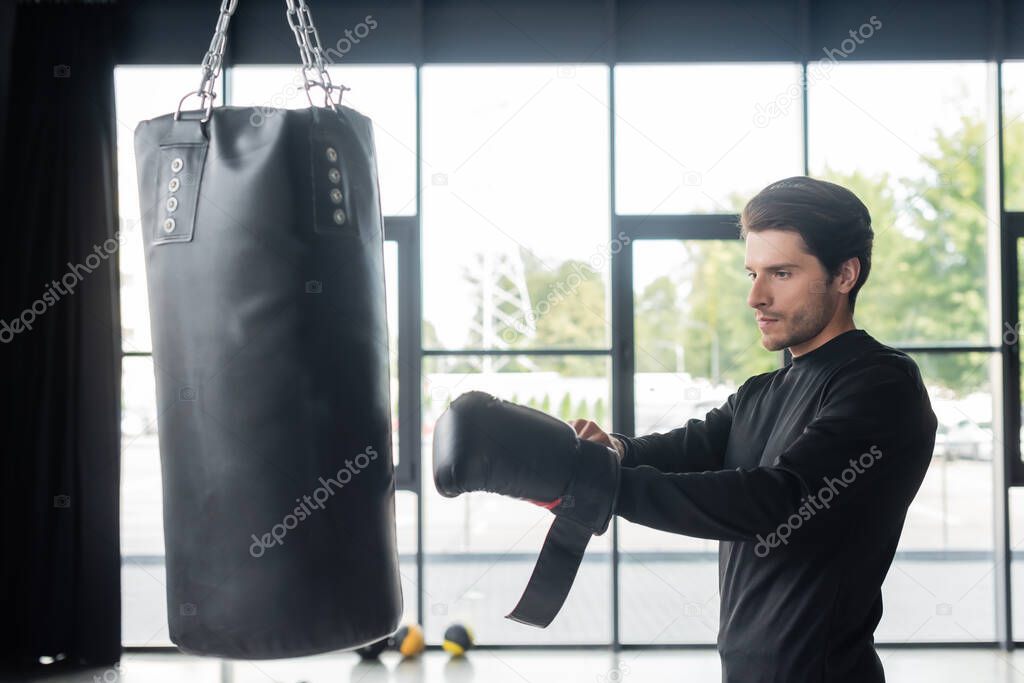 Brunette boxer wearing glove near punching bag in sports center 