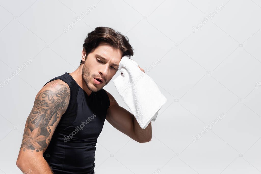 Tired sportsman wiping face with towel isolated on grey 