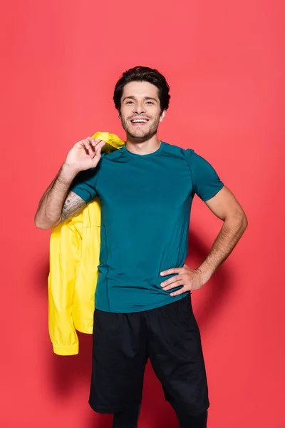 Positive Sportsman Holding Yellow Sports Jacket Hand Hip Red Background — Stockfoto