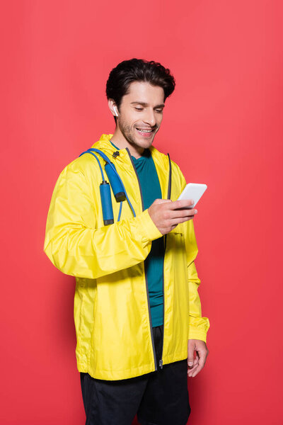 Мужчина в наушниках и на спортивной куртке держит смартфон на красном фоне 