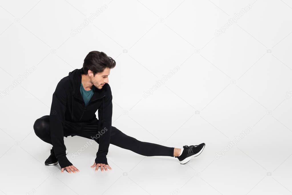 Brunette sportsman stretching on grey background 