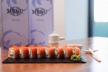 tasty sushi rolls with red caviar and wasabi near blurred menu brochures on wooden table