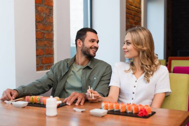 Suşi barında yemek yerken birbirlerine bakan neşeli bir çift.