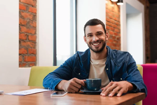 Hombre Alegre Mirando Cámara Cerca Taza Café Teléfono Inteligente Con — Foto de Stock