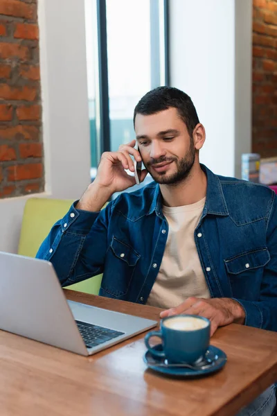 Smiling Man Talking Mobile Phone Laptop Blurred Coffee Cup Cafe — Fotografia de Stock