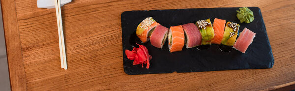 top view of delicious sushi rolls with sesame near chopsticks on wooden table, banner