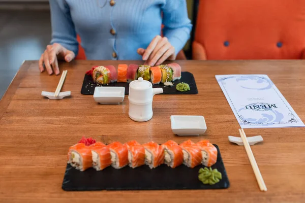 Cropped View Blurred Woman Menu Plates Sushi Rolls Chopsticks Soy — Fotografia de Stock