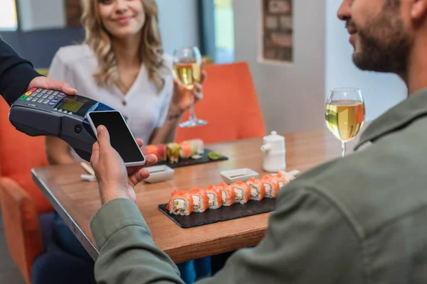 男子与女子在寿司酒吧约会期间在付款终端附近手持智能手机的剪影 — 图库照片