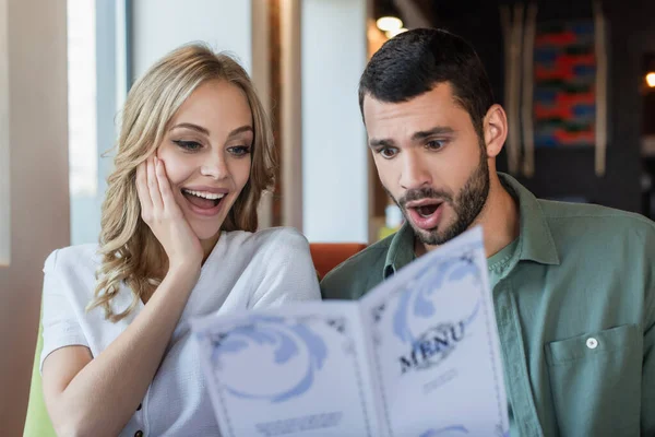 Σοκαρισμένη Γυναίκα Αγγίζοντας Πρόσωπο Ενώ Διαβάζοντας Εστιατόριο Μενού Κοντά Έκπληκτος — Φωτογραφία Αρχείου