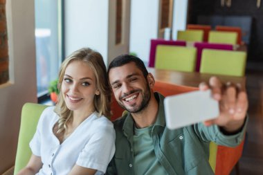 Kafedeki bulanık cep telefonundan selfie çeken neşeli çift.