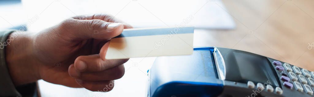 cropped view of man holding credit card near payment terminal in cafe, banner