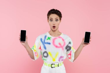 Şaşırmış esmer kadın pembe ekranda boş ekranlı akıllı telefonlar gösteriyor.