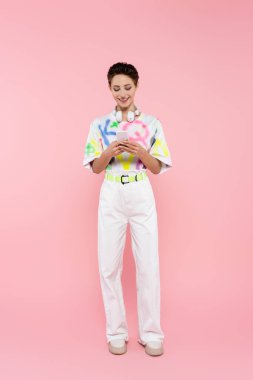 Kablosuz kulaklıklı, pembe kulaklıklı, akıllı telefondan konuşan, gülümseyen bir kadın.