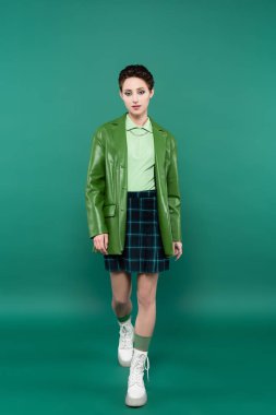 Deri ceketli, ekose etekli, yeşil çizmeli, şık bir kadın.
