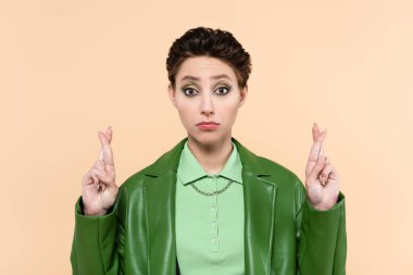 Yeşil deri ceketli, cesareti kırılmış bir kadın bej renkli parmaklarını çapraz tutuyor.